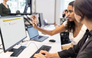 Two women in an office, accessing the Clinical Trial Management System program on a computer monitor.