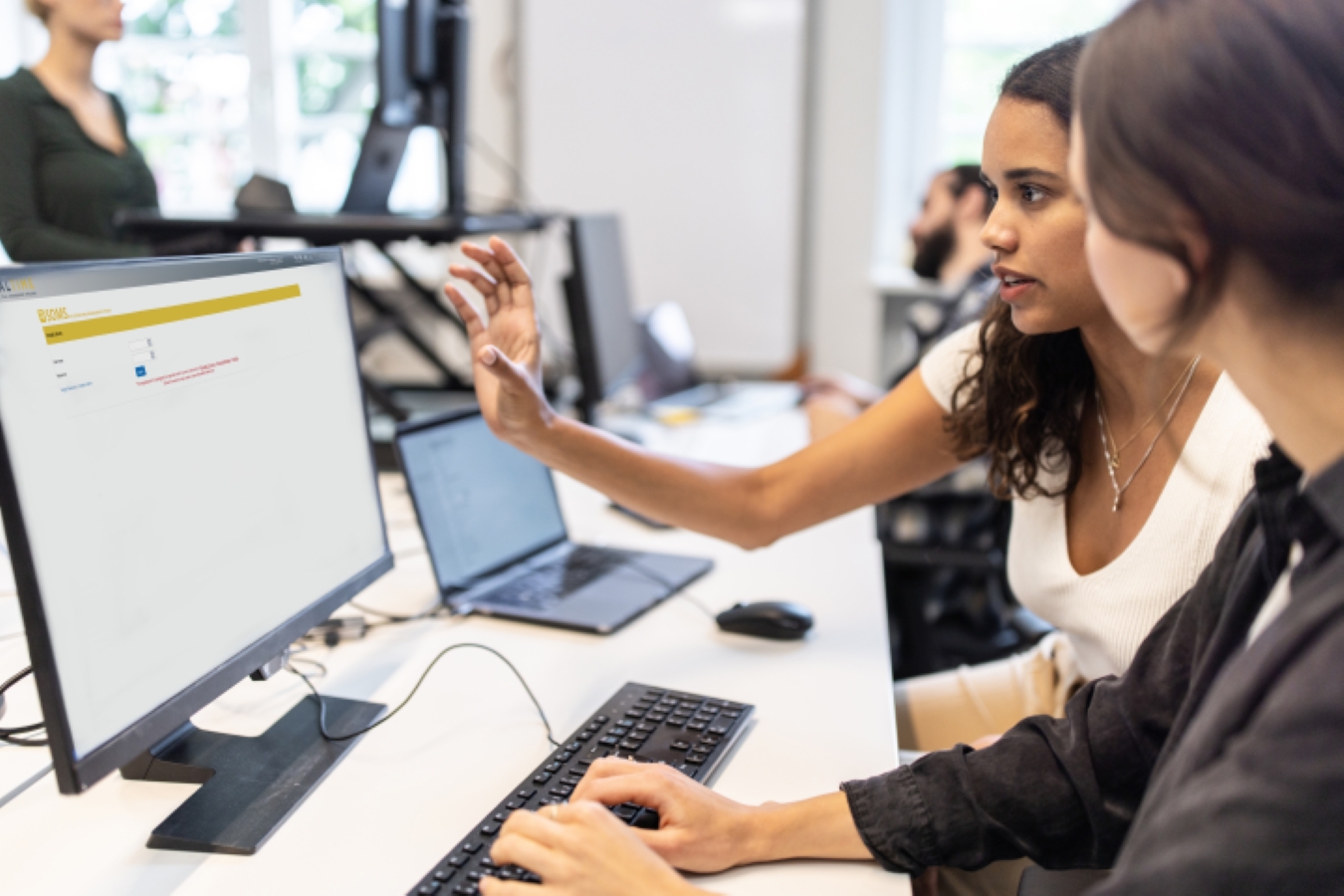 Two women in an office, accessing the Clinical Trial Management System program on a computer monitor.