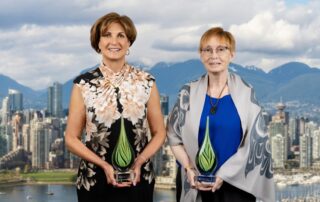Two recipients of the Clinical Trials British Columbia Awards 2026, smiling and standing against a city skyline while holding glass awards.