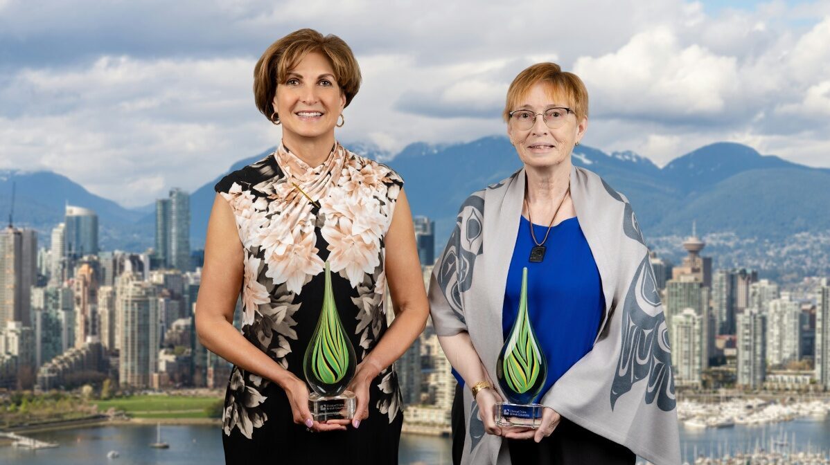 Two recipients of the Clinical Trials British Columbia Awards 2026, smiling and standing against a city skyline while holding glass awards.